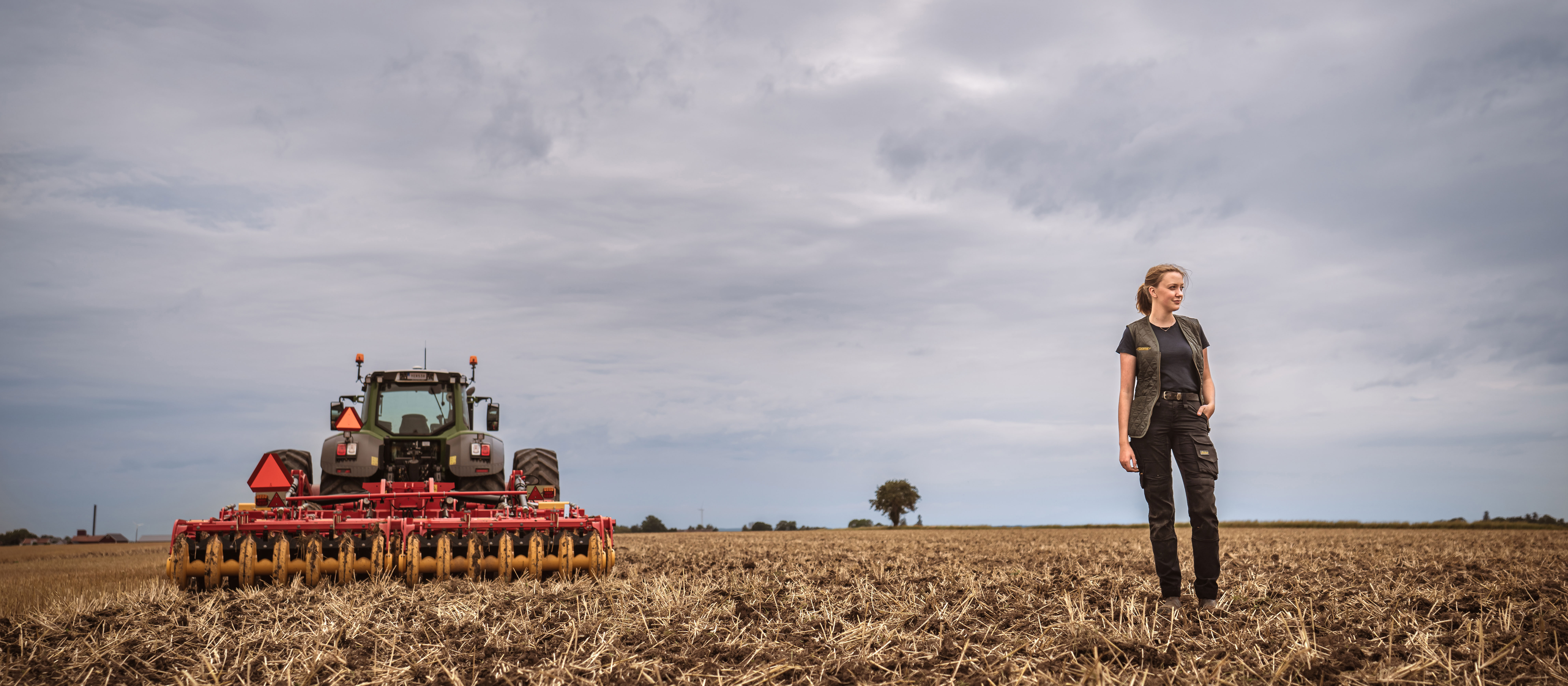 A girl and a red tillage machine standing in the field.